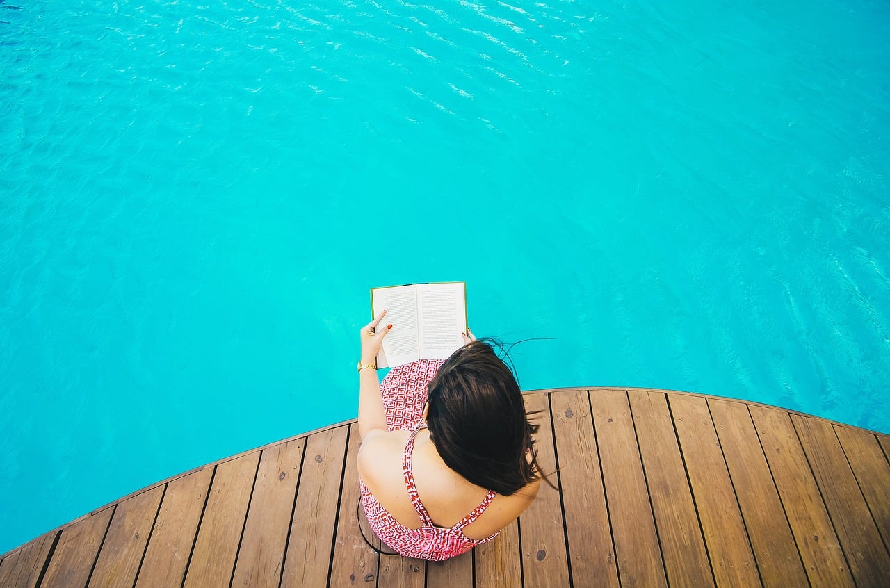 Femme en bord de piscine avec un livre