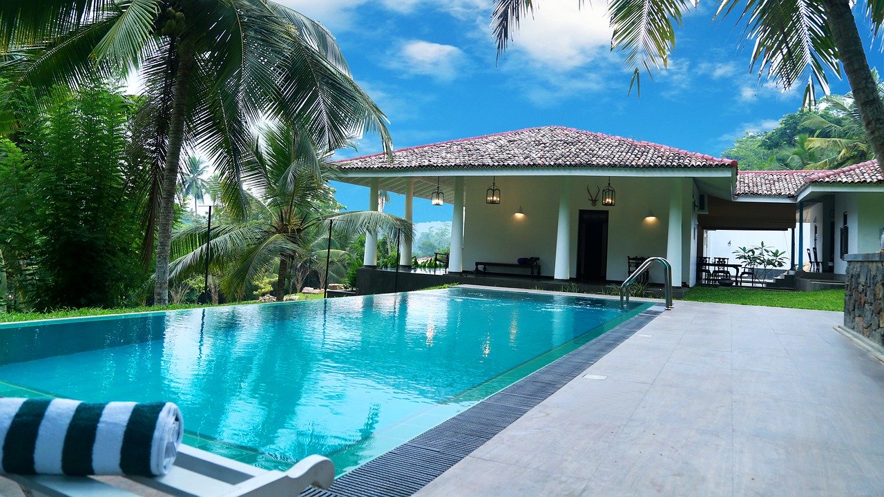 Piscine devant maison blanche à piliers entourée de cocotiers